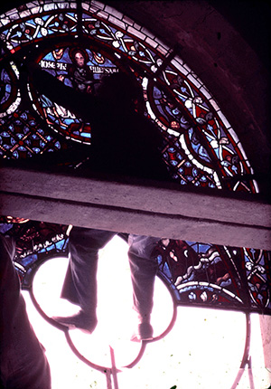 Robert Metcalf seated on scaffolding photographing stained glass