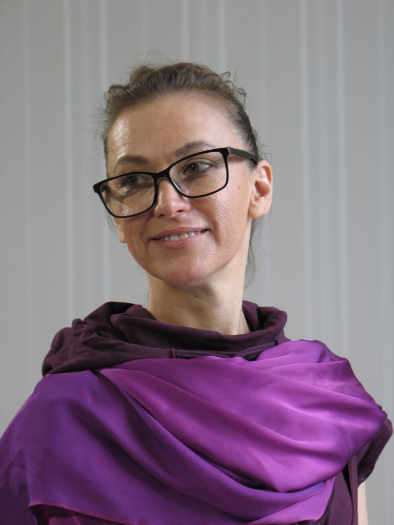 A woman with her hair pulled back, wearing glasses and a purple scarf.