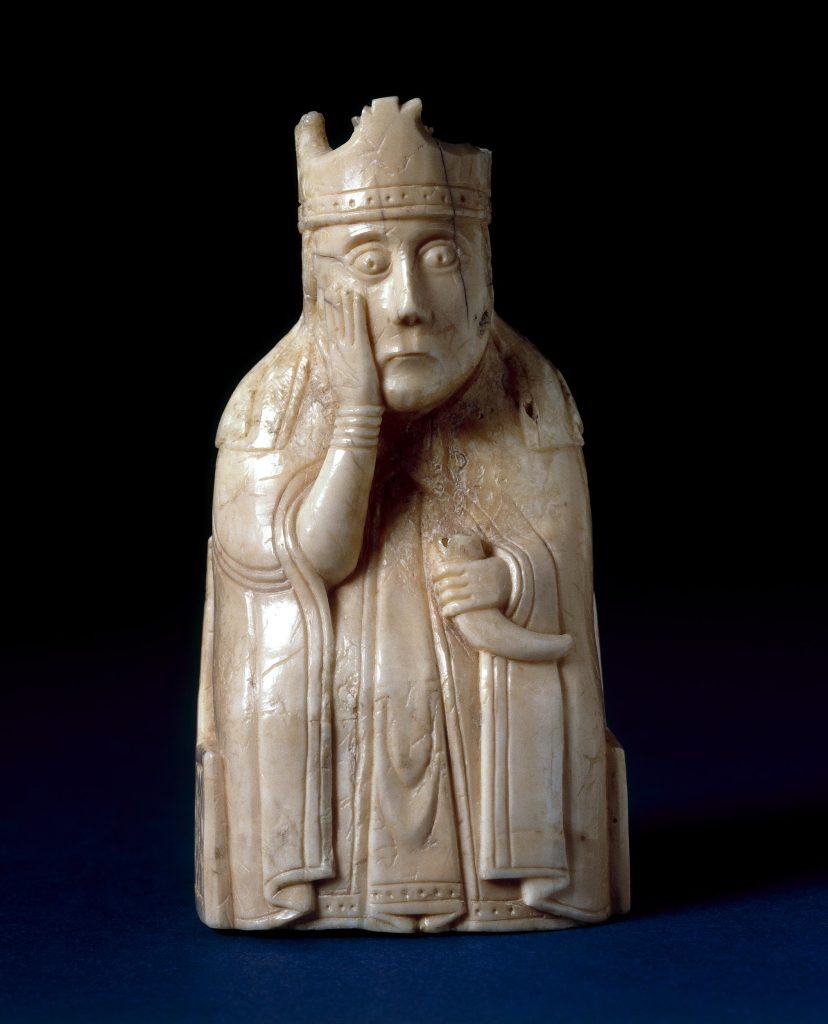 An ivory statuette of a crowned, seated woman holding a curved horn in her left hand and holding her right hand to her cheek.