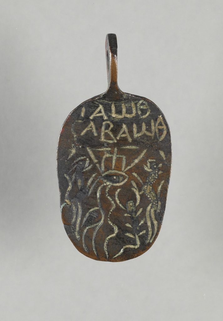 A bronze oval amulet with a suspension loop at the top, engraved with a Greek inscription, an evil eye, a trident, a lion, an ibis, a snake, a scorpion, a leopard and spears.