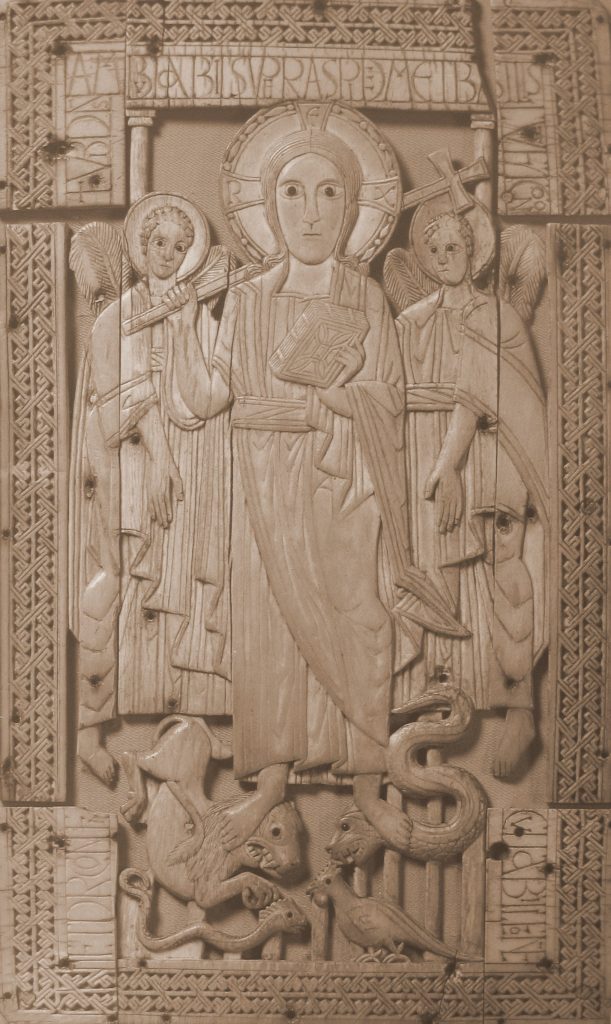 A rectangular ivory panel depicting a man with a crossed halo and holding a cross-staff and book, flanked by two angels holding staffs, trampling a lion and a serpent underfoot. Another serpent and cock in the foreground, inscriptions, and a geometric border. Some surface cracks and holes.